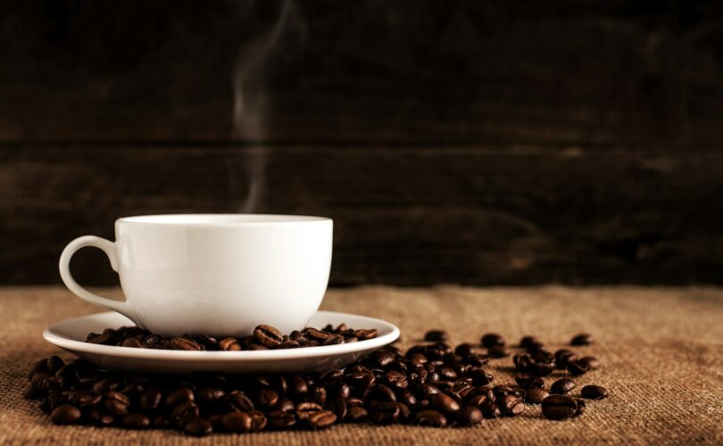 white ceramic mug and saucer with coffee beans on brown textile